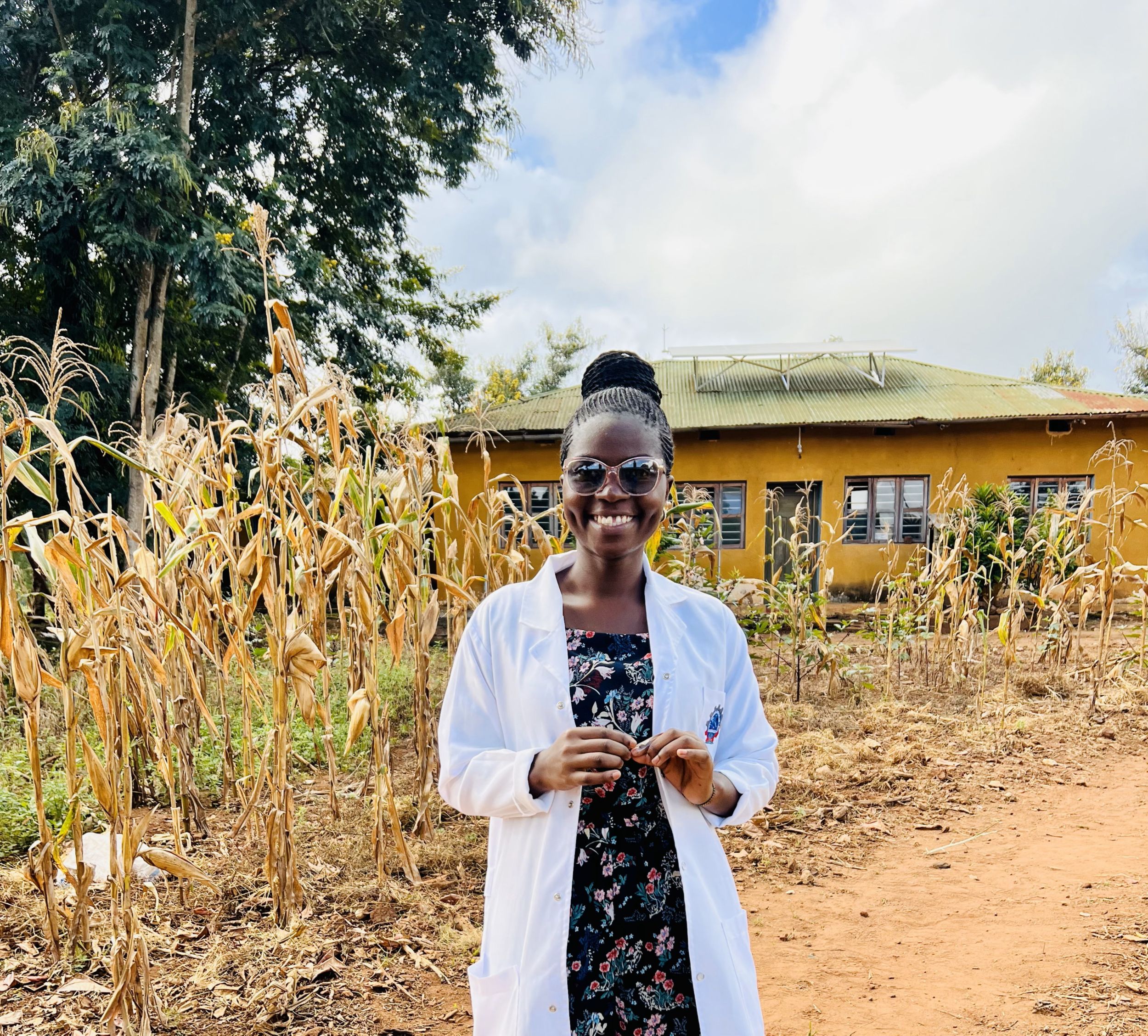 A female doctor stands in front of a remote health clinic on a sunny day.