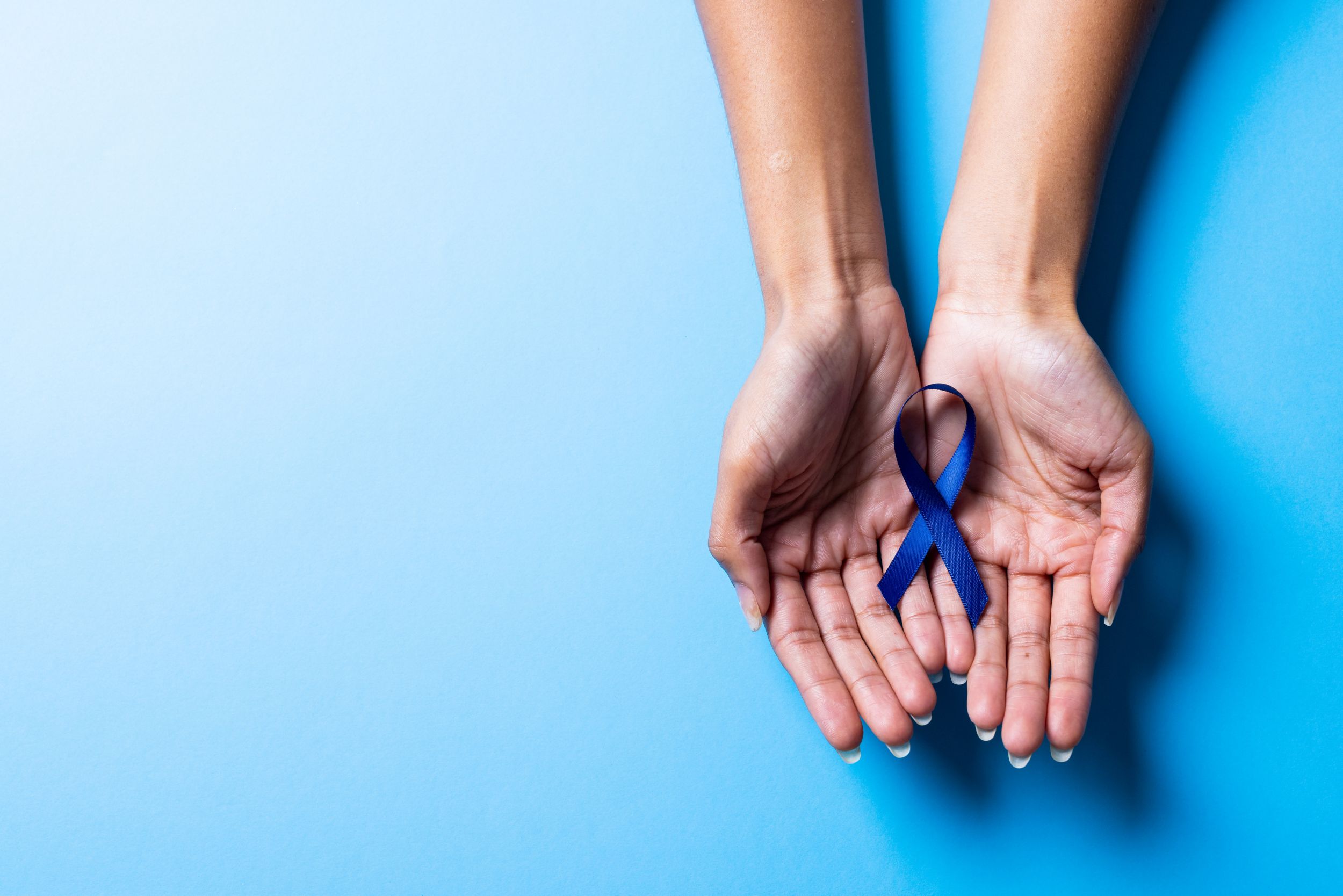 closeup of hands holding a dark blue awareness ribbon on a light blue background
