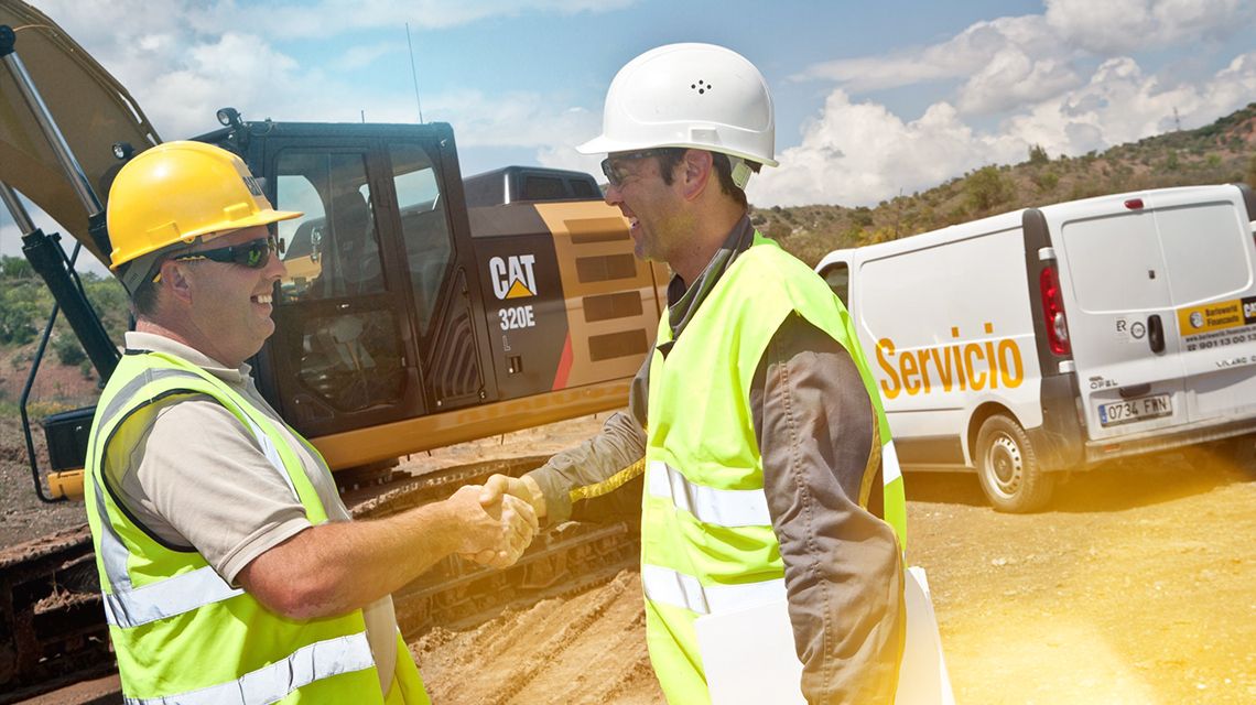 Two men shaking hands in front of a 320E Excavator and Service Vehicle