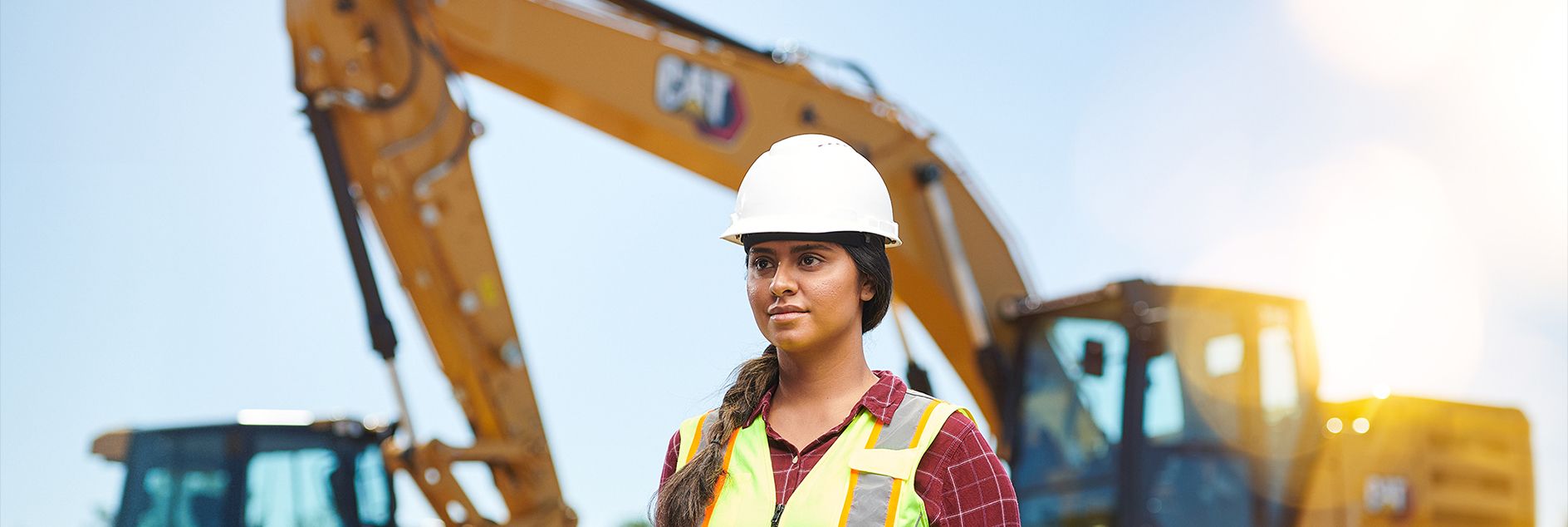 Mulher em frente a uma escavadeira usando capacete