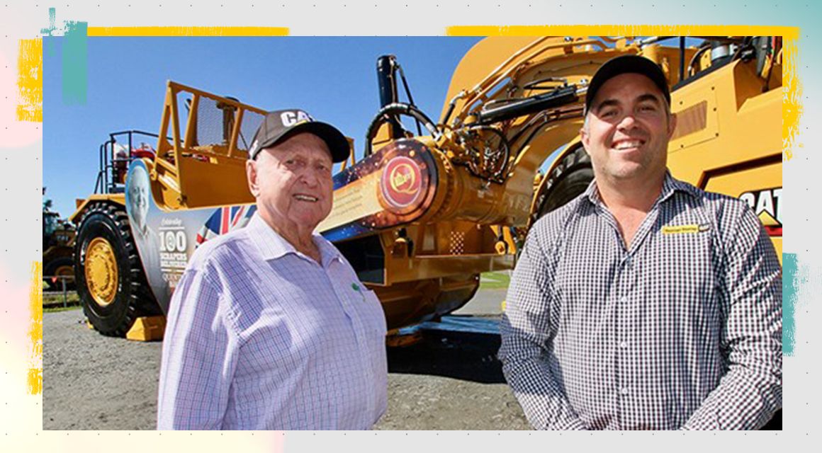 Two men smiling in front of a Cat machine