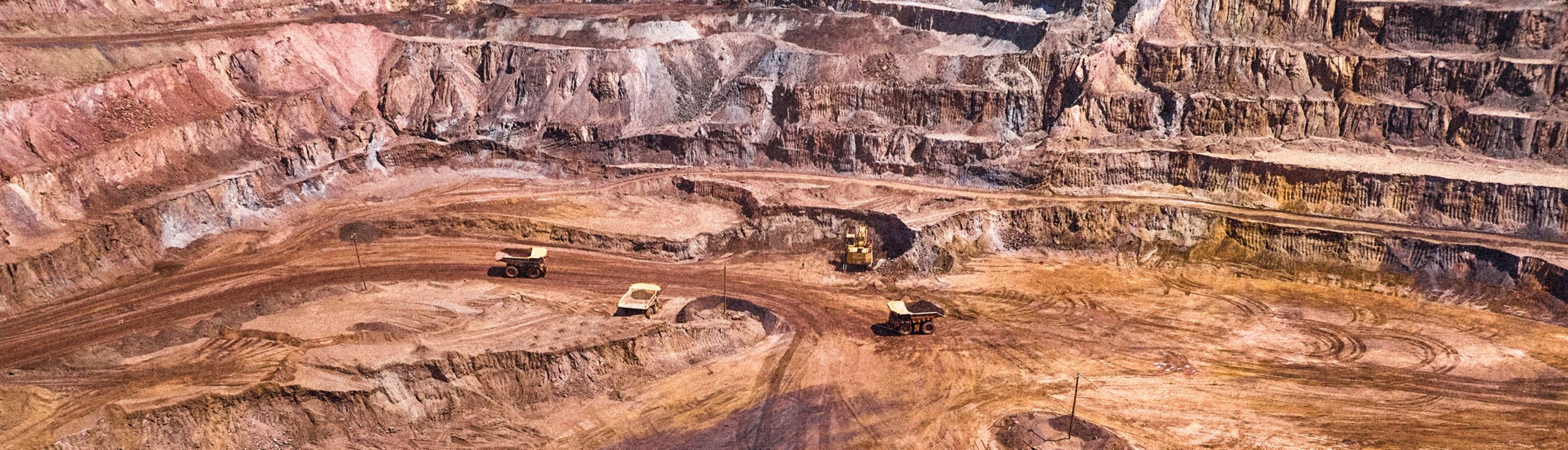 mining site with 3 large mining trucks and and large excavator in the distance