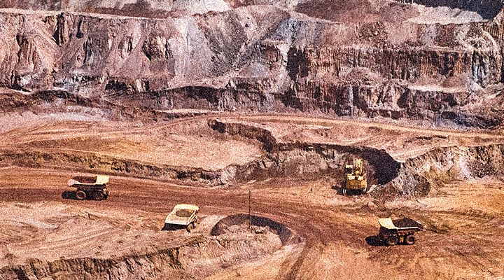 mining site with 3 large mining trucks and and large excavator in the distance