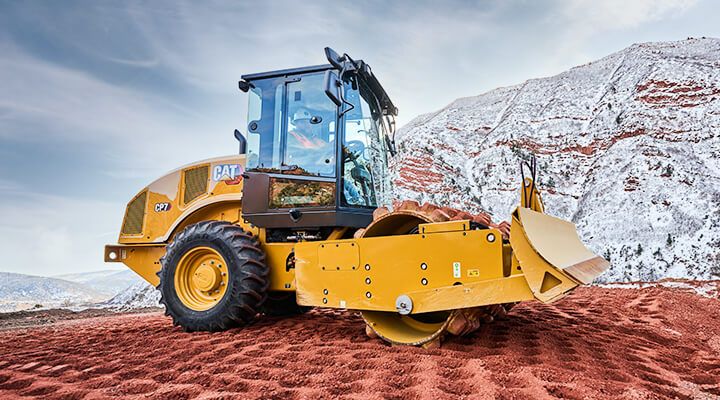 Soil compactor on red terrain in front of snowy pile of dirt