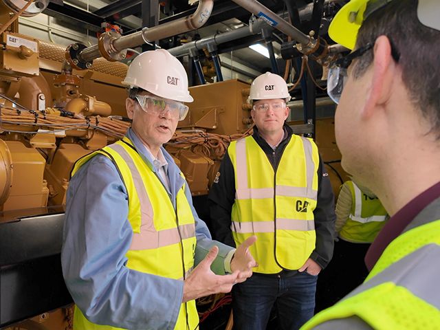 3 workers talking in front of a Cat generator