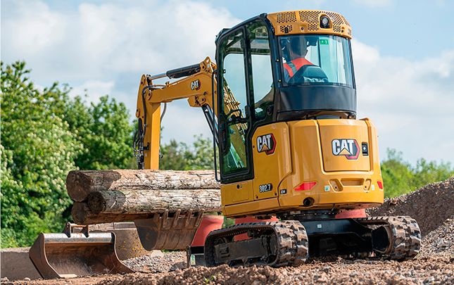 Mini escavadeira usando um acessório de caçamba para levantar toras