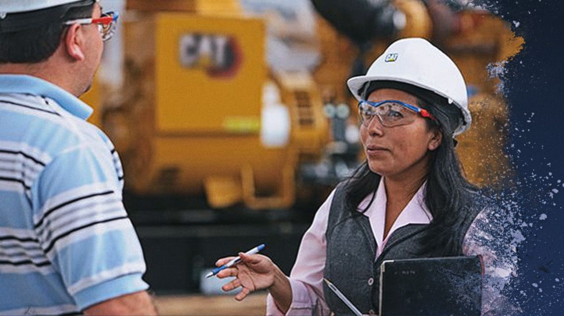 Two people talking in front of Cat equipment