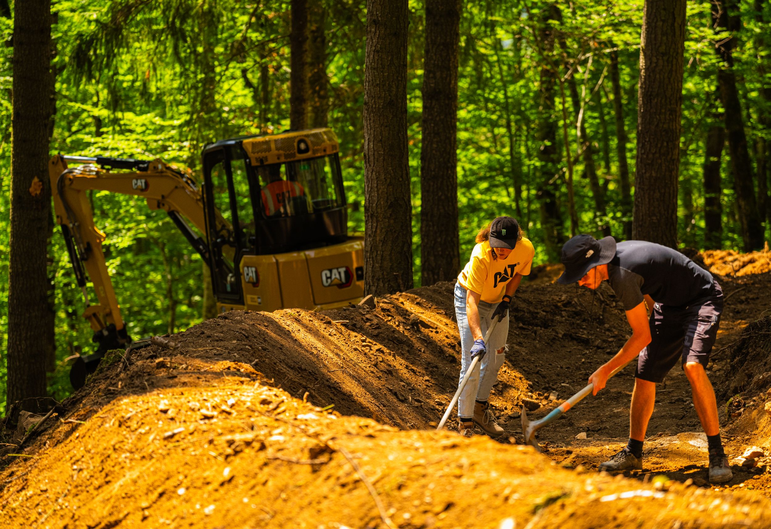Cat 306 Minibagger mit Cat-Löffeln beim Bau von 300 m neuen Mountainbike-Strecken in steilem Waldgelände in Frankreich.