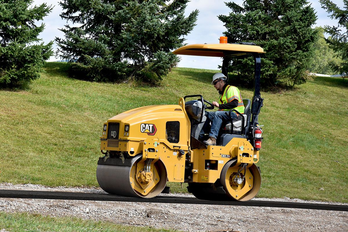 Un trabajador de la construcción en un compactador de servicios públicos pavimentando una nueva carretera.