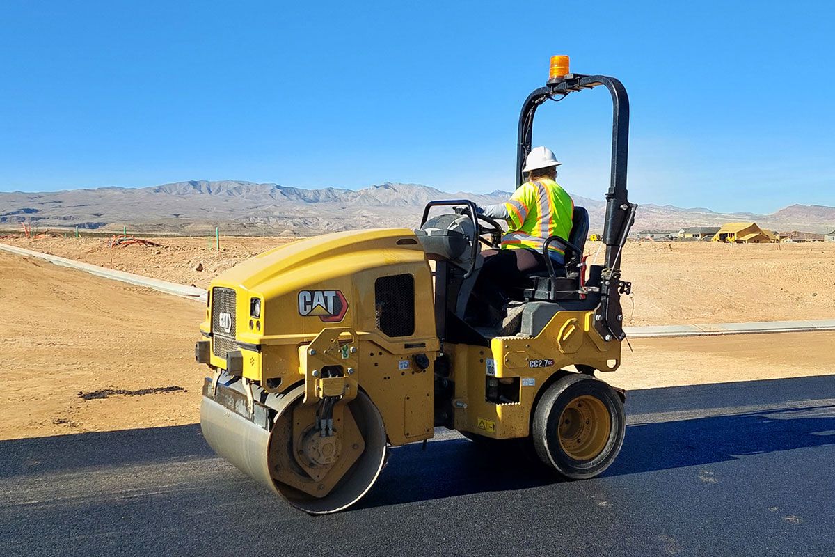 Un trabajador de la construcción en un compactador de servicios pavimentando una nueva carretera en el desierto