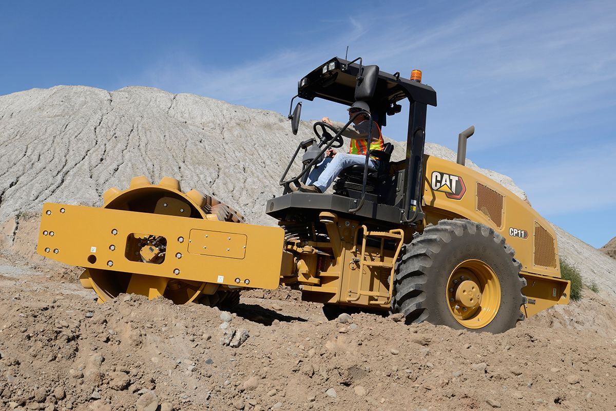 Hombre subiendo una pendiente en un compactador de suelo vibratorio Caterpillar CP11