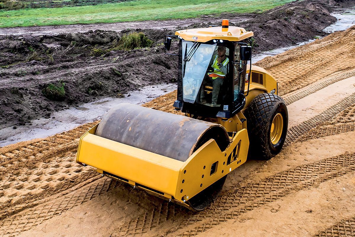 Hombre en un compactador vibratorio Caterpillar CS11 GC en un camino de tierra