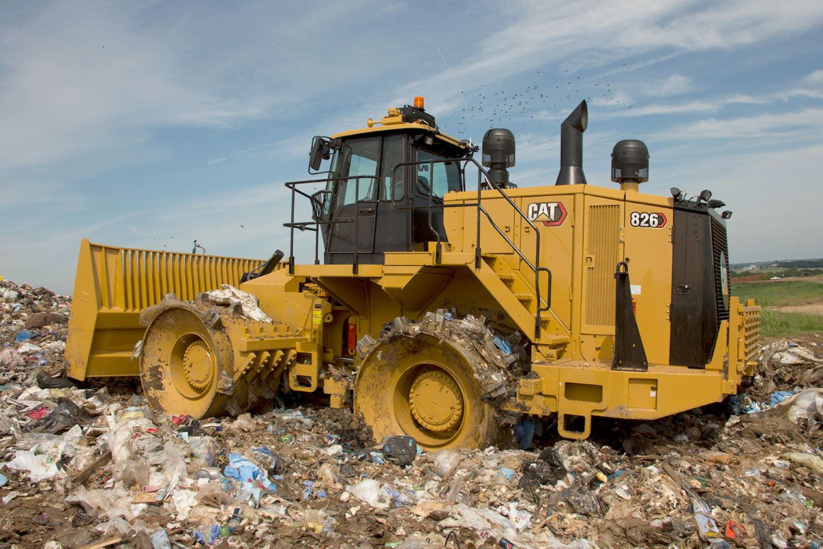 Un compactador de basura atravesando un vertedero limpiando basura
