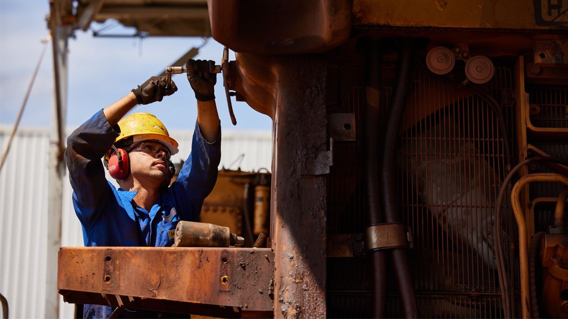 Man inspecting underside of cat mining machine