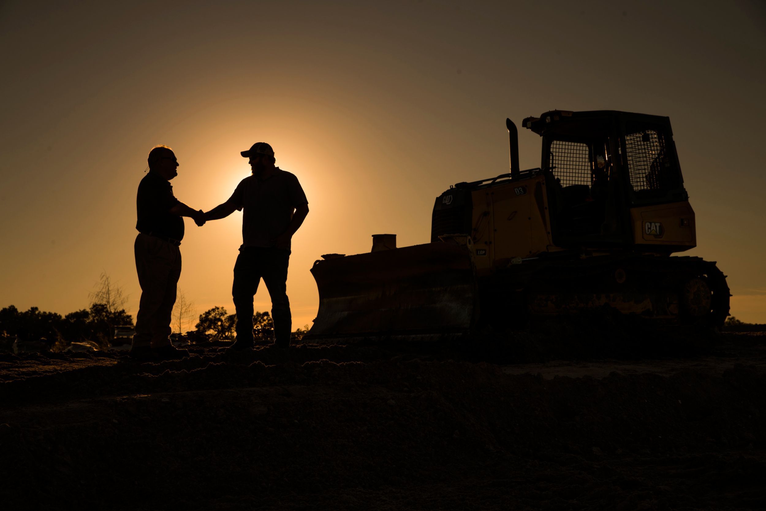 two people shaking hands near a dozer