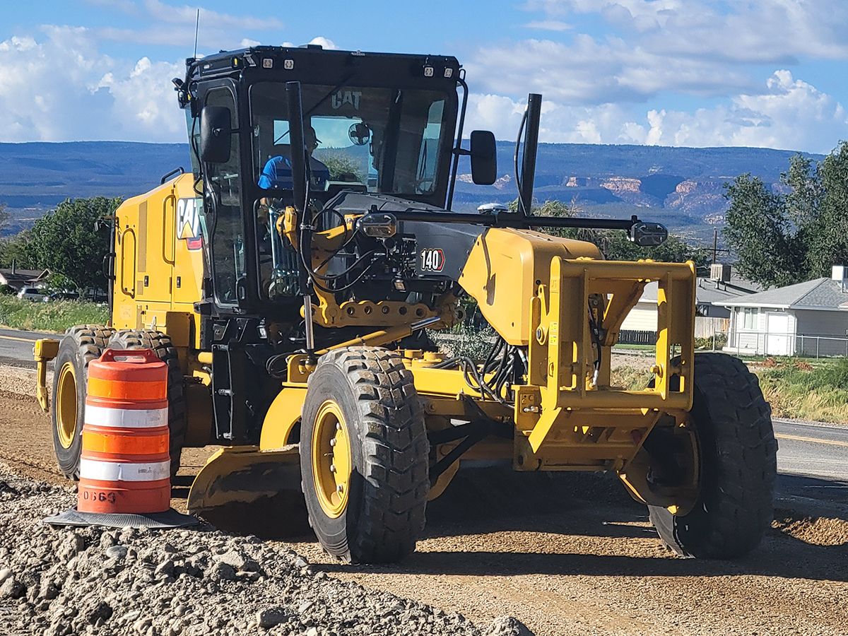 140 motor grader grading a road next to an orange construction cone in the mountains