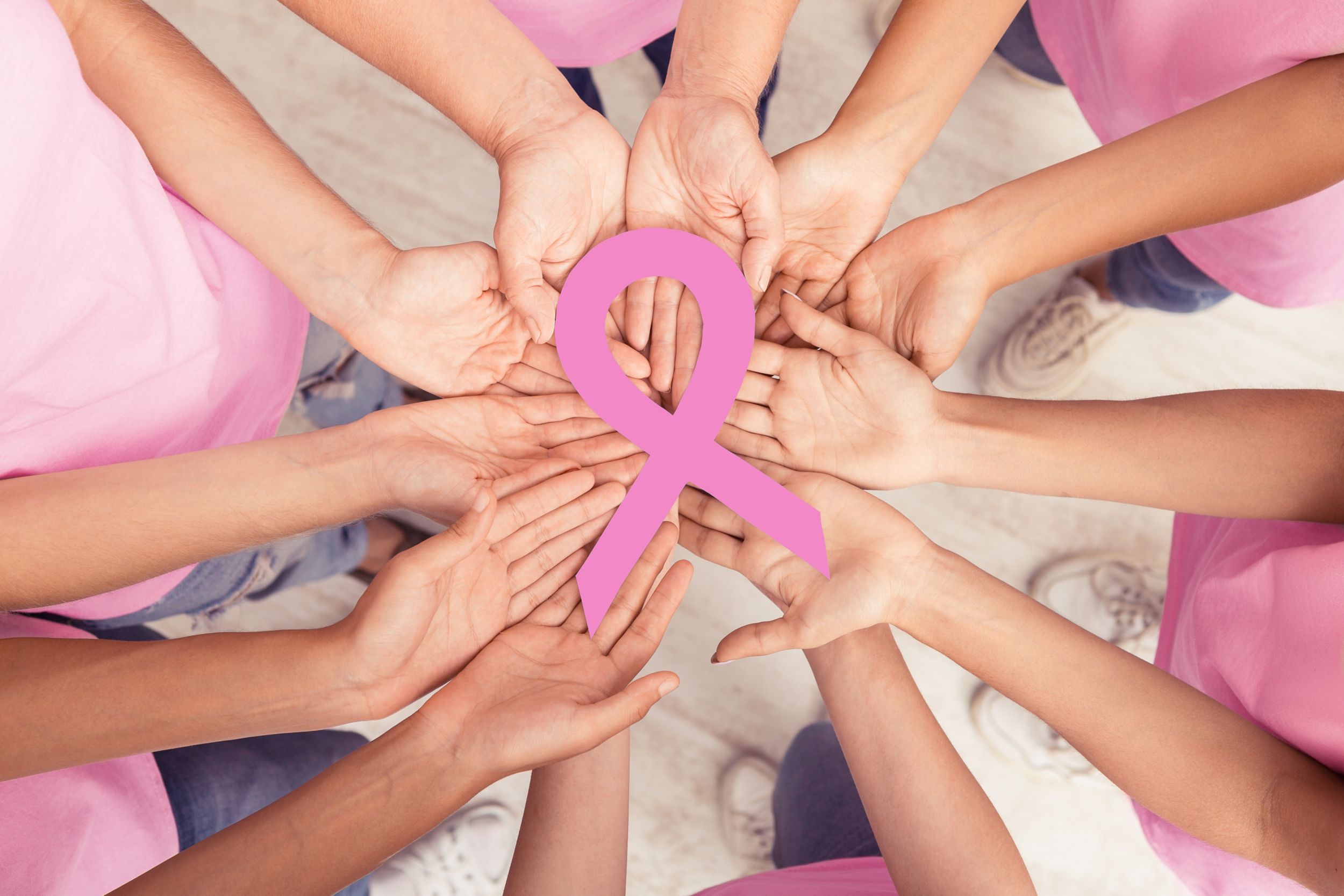Many women's hands holding a pink awareness ribbon