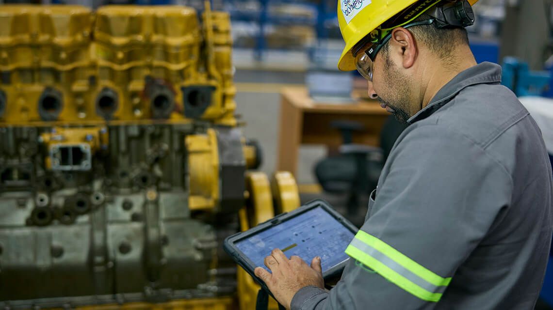 technician checking the status on a tablet with an engine in the background