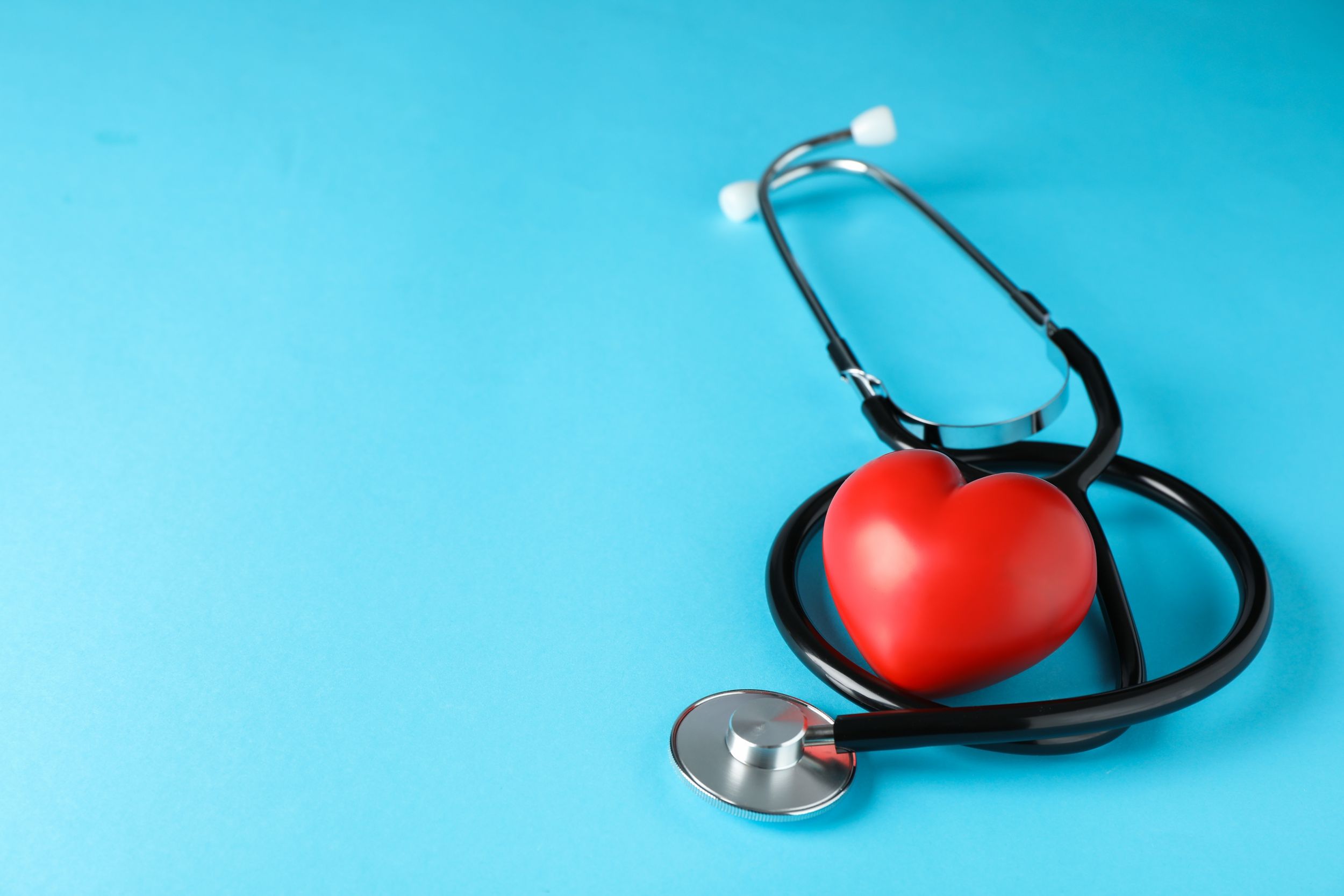 A stethoscope wrapped around a heart-shaped stress ball in front of an aqua blue background