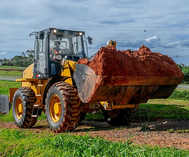 Cargadoras compactas Cat® moviendo tierra en un campo de césped.