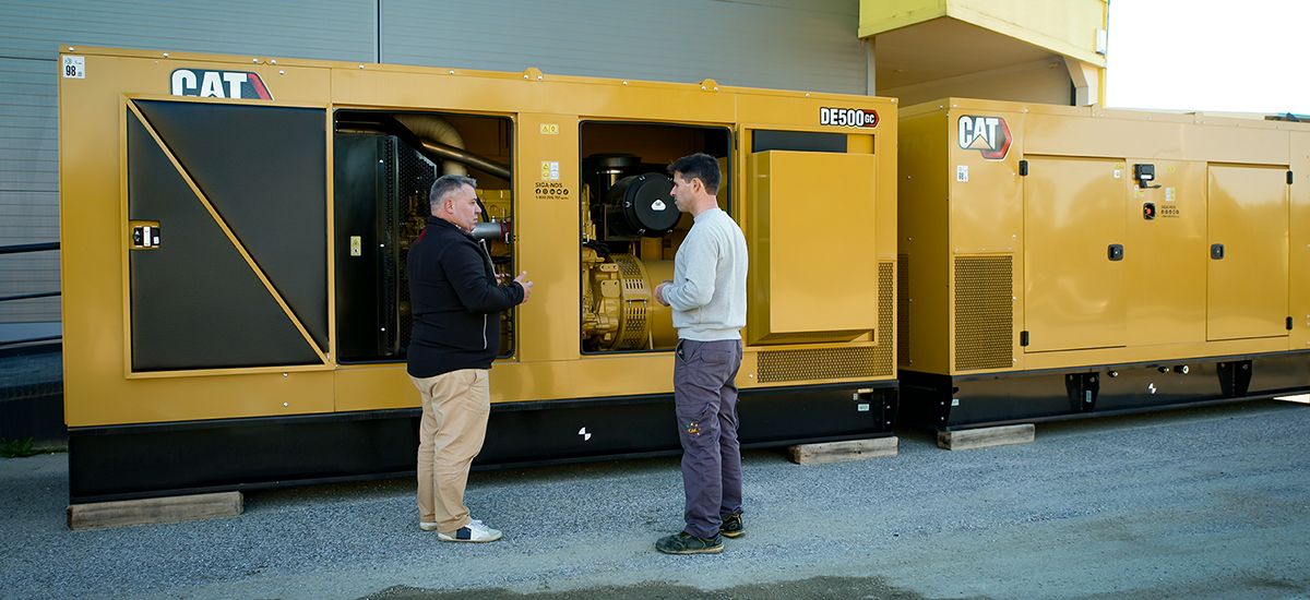 Two men talking in front of two enclosed Cat DE500 CG diesel gensets in the background