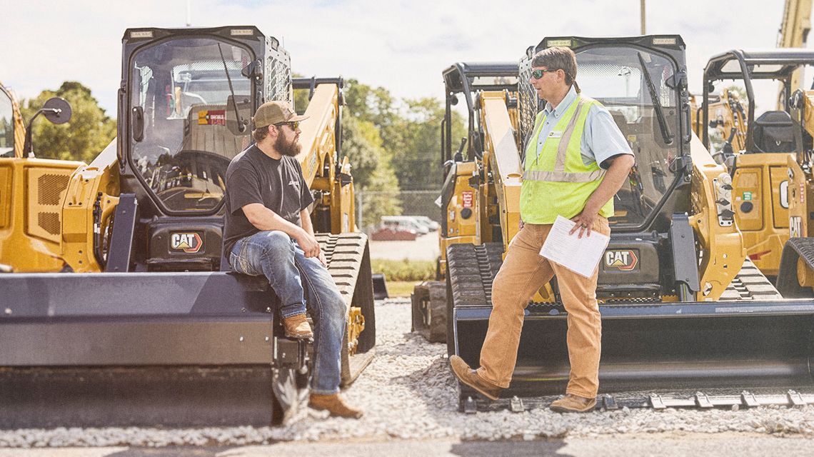 two men talking in front of compact track loaders
