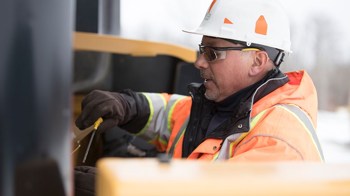 operator in a vest and hardhat making adjustments to a machine