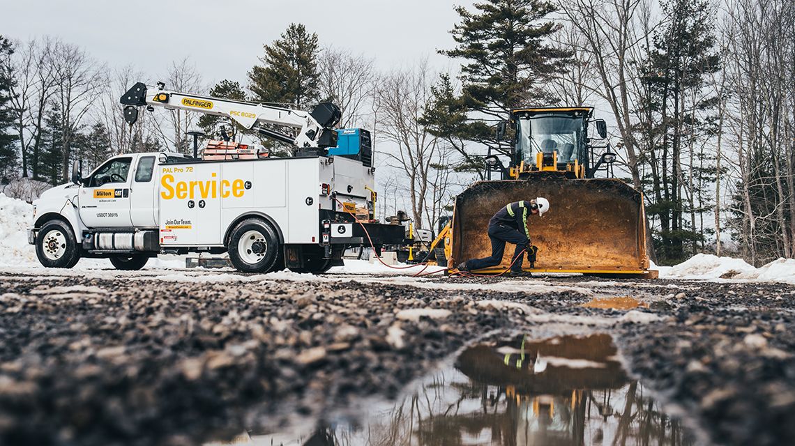a technician adjusting the bucket of a machine; service truck next to them