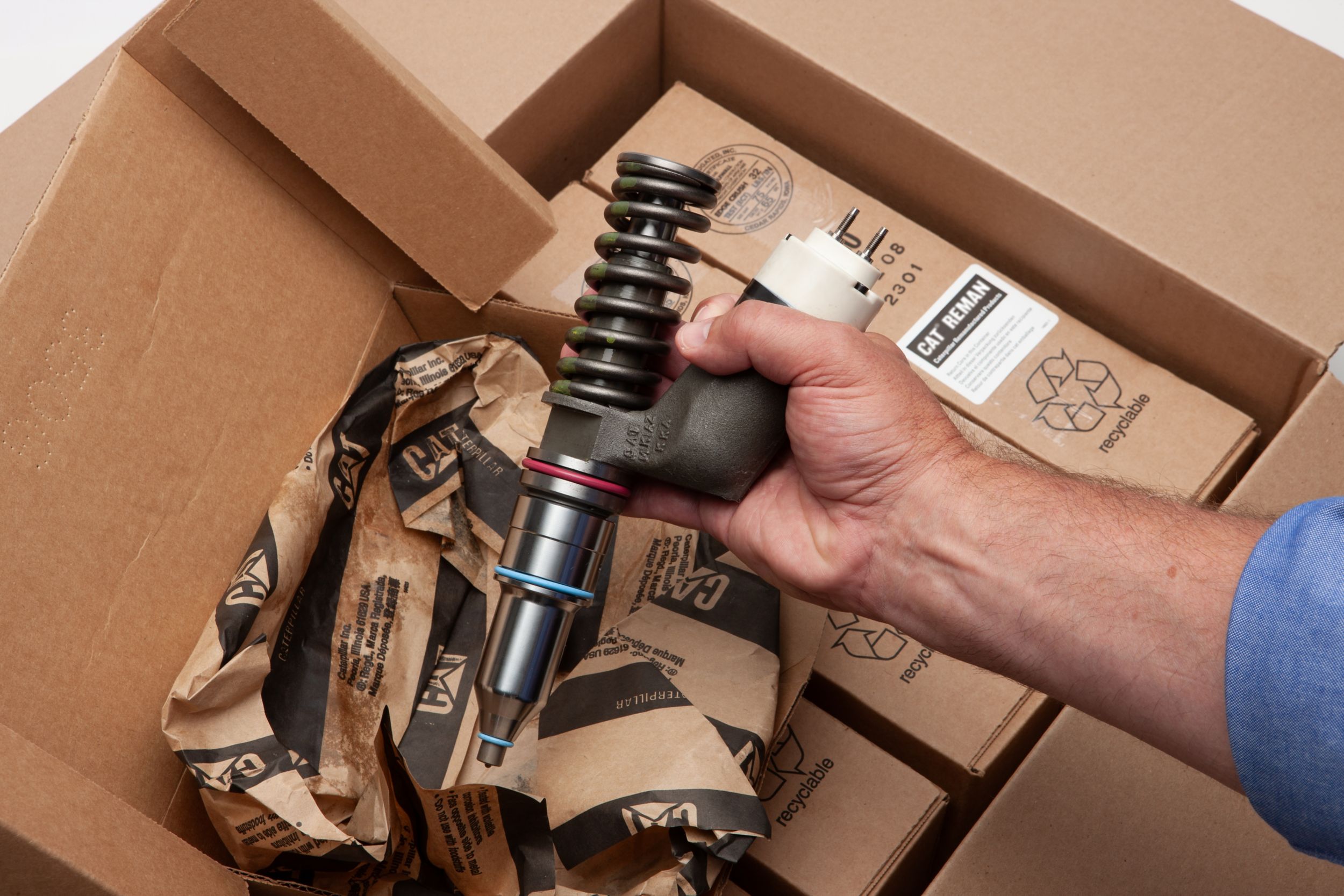 a hand unboxing a remanufactured injector with cardboard boxes in the background