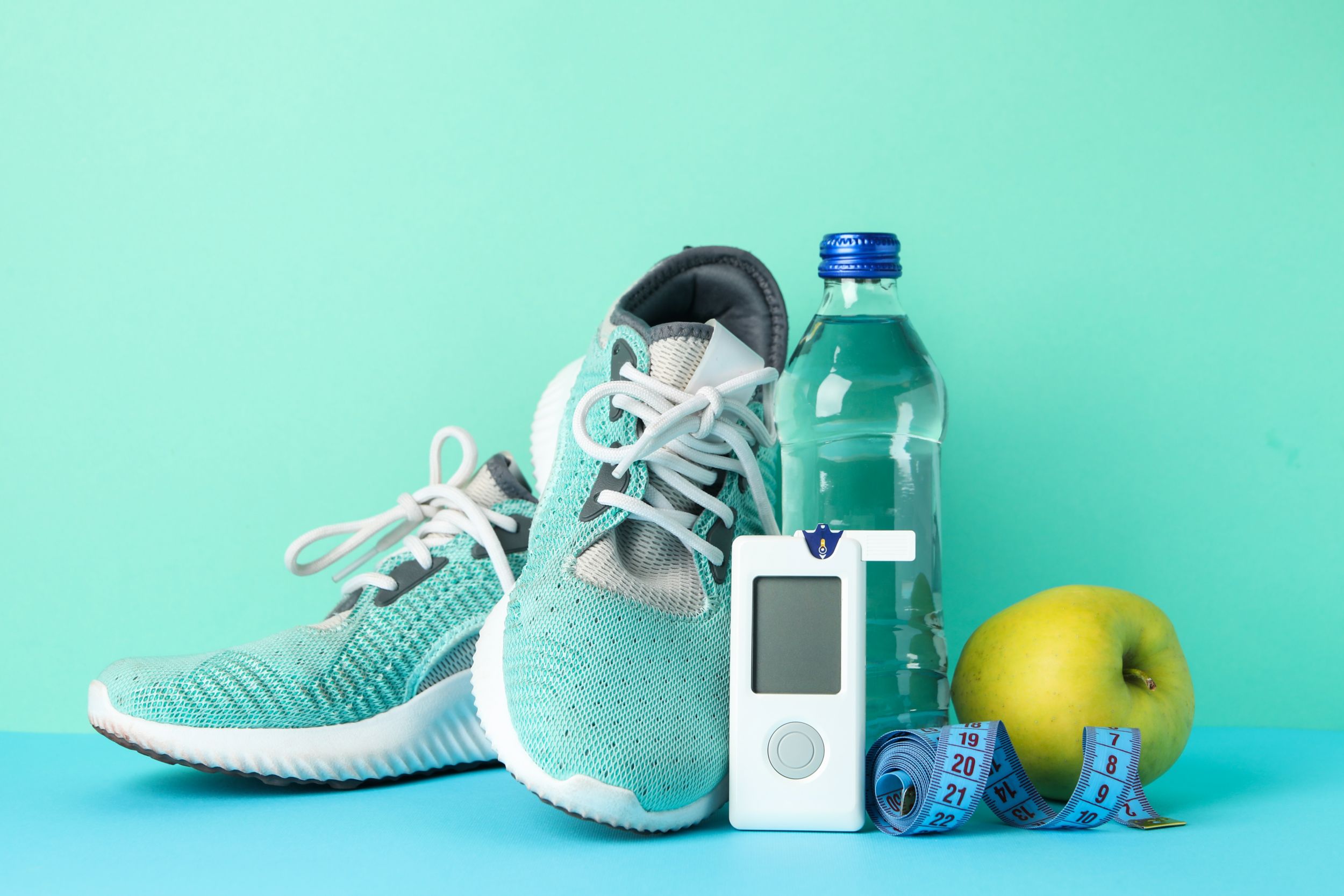 Sneakers, water bottle, apple, tape measure, and glucometer on a mint background
