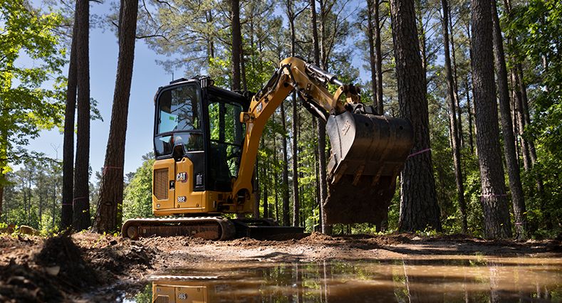 Una pequeña excavadora utilizando su cuchara en el bosque.