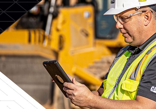 A Cat representative looking at a mobile device in front of a Cat machine