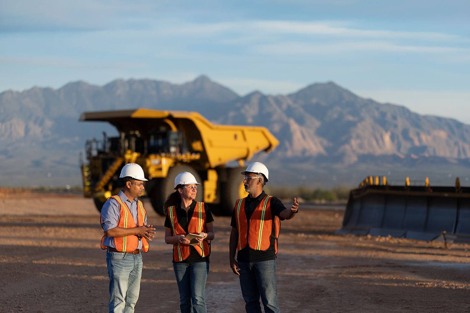 Three people in PPE talking in front of a Cat® 793 mining truck