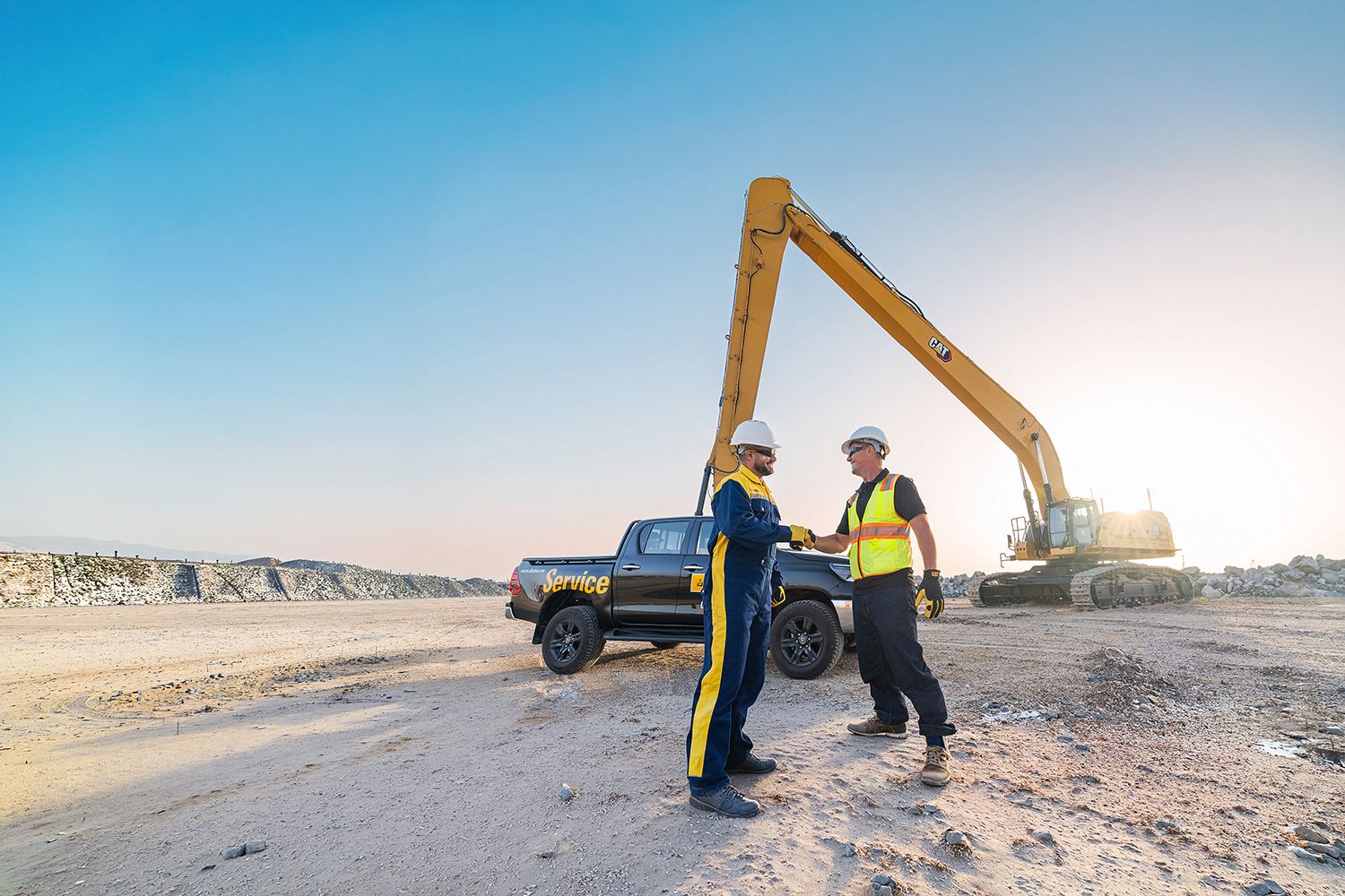 A technician and a customer shaking hands in front of an excavator.