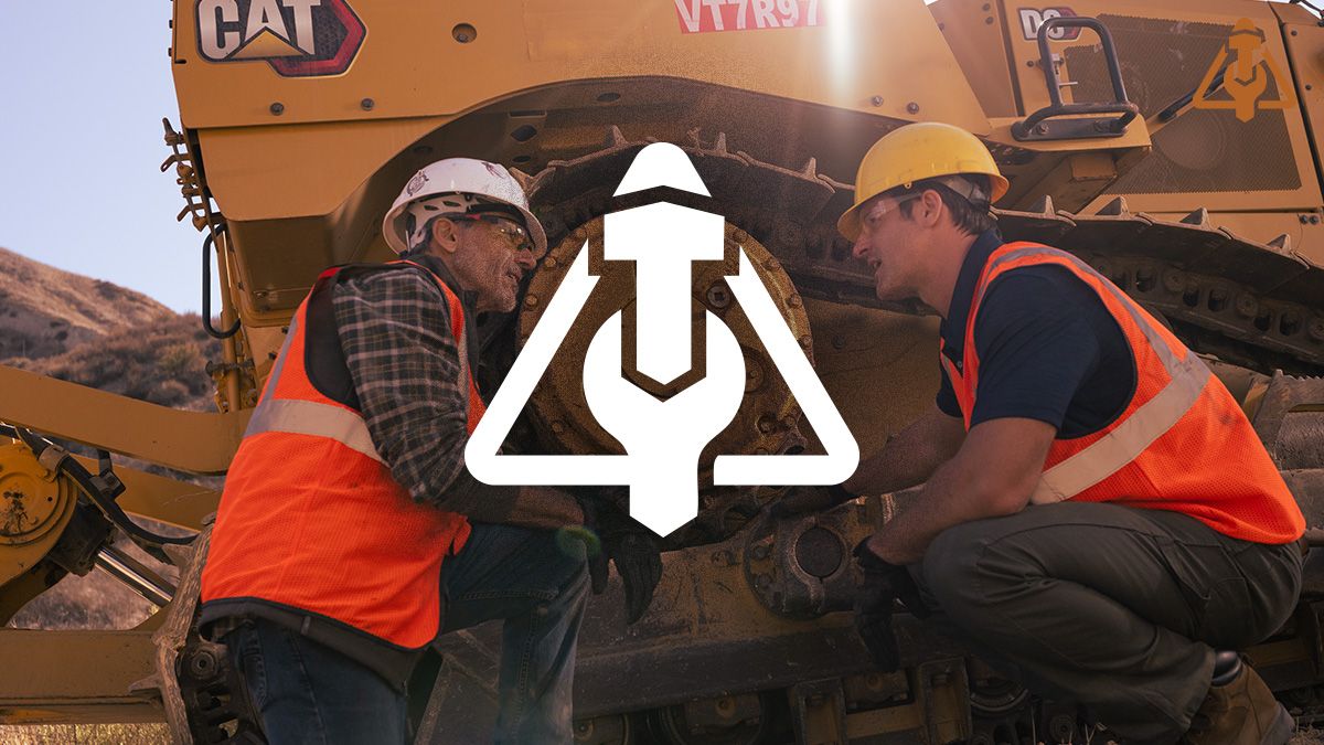 Two CAT technicians in safety gear kneel while inspecting a Caterpillar machine component outdoors.