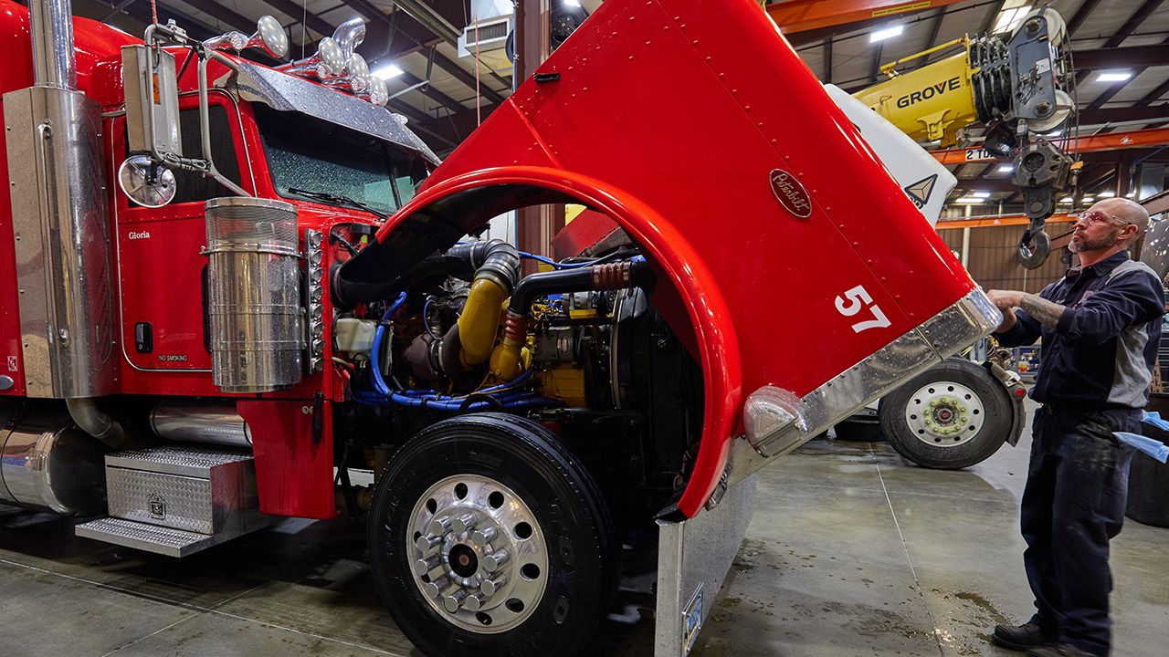 Technician opening the hood of a semi-truck, revealing yellow Cat engine