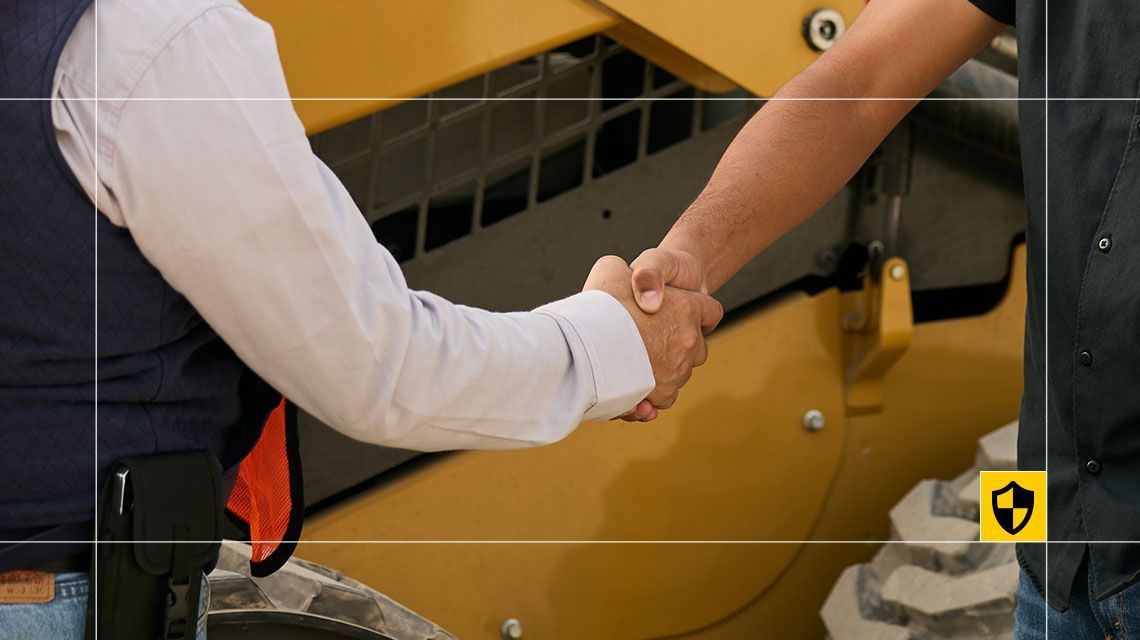 Two men shaking hands in front of Cat equipment