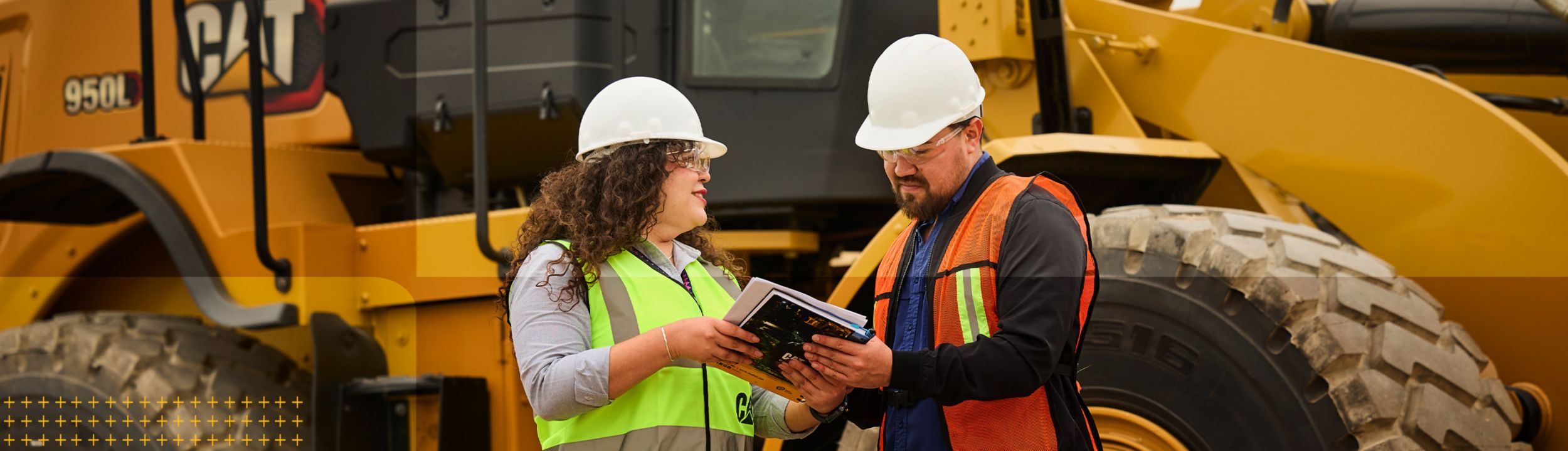 Two workers standing in front of Cat equipment sharing CVA information