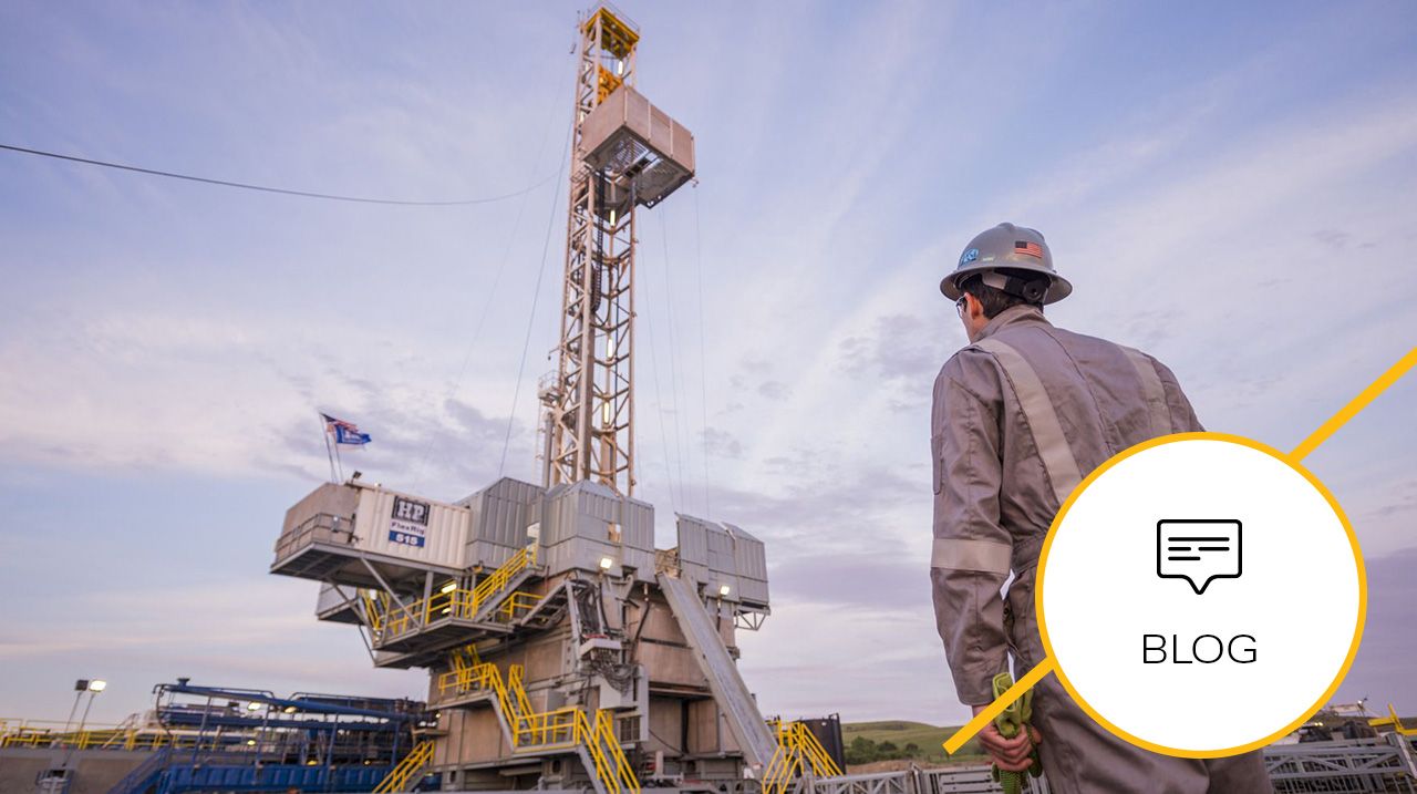 Back of a worker in a hardhat overlooking a land drilling rig under an expansive sky