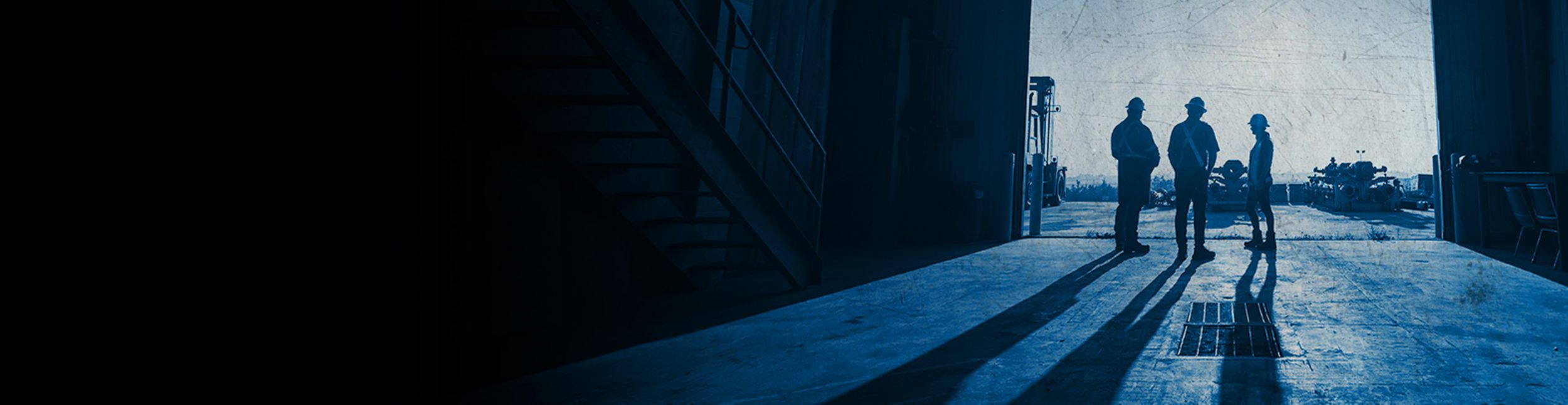 Three workers standing in a warehouse with their shadows cast across the floor