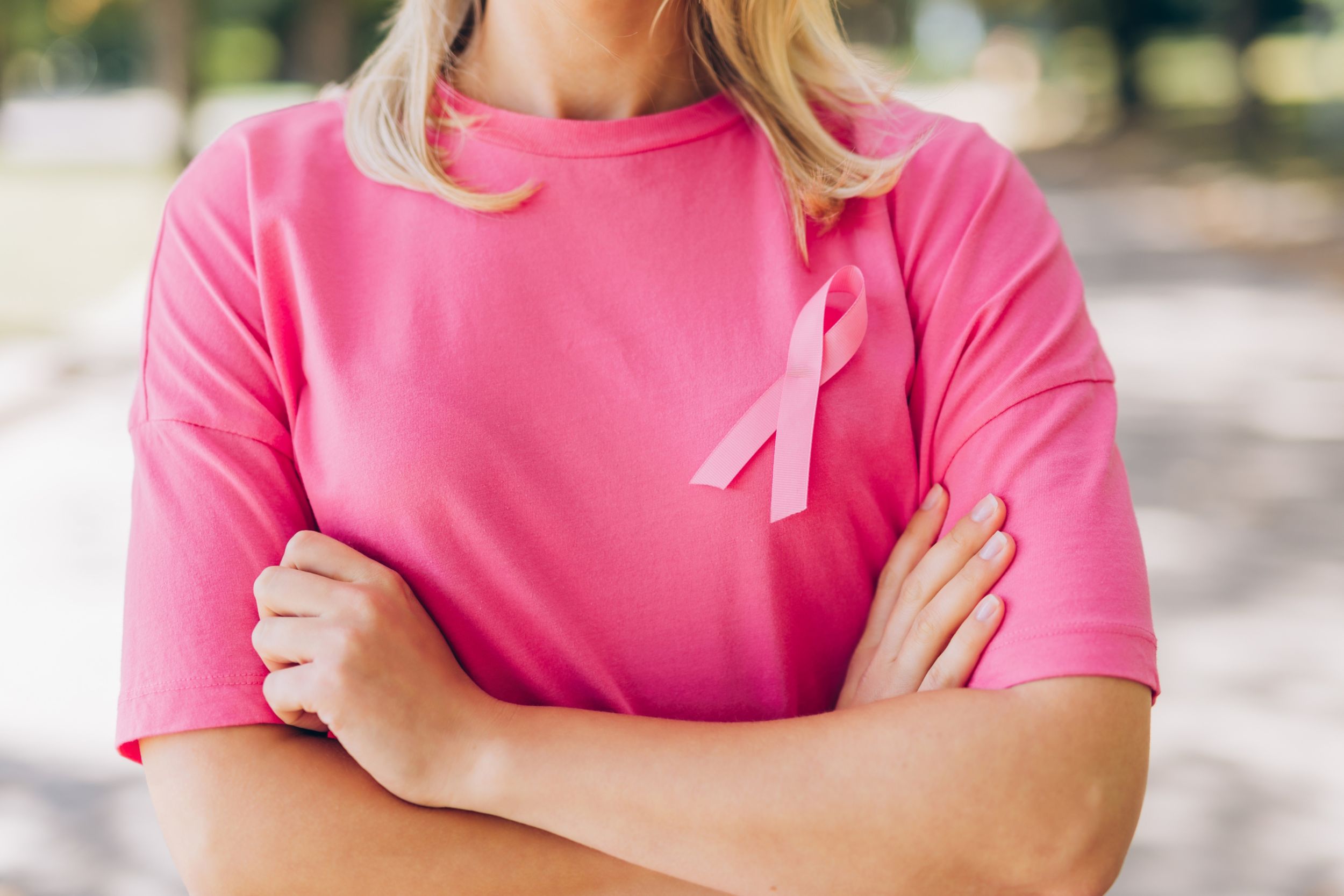 A closeup of a person wearing a pink t-shirt with a pink ribbon to represent breast cancer awareness