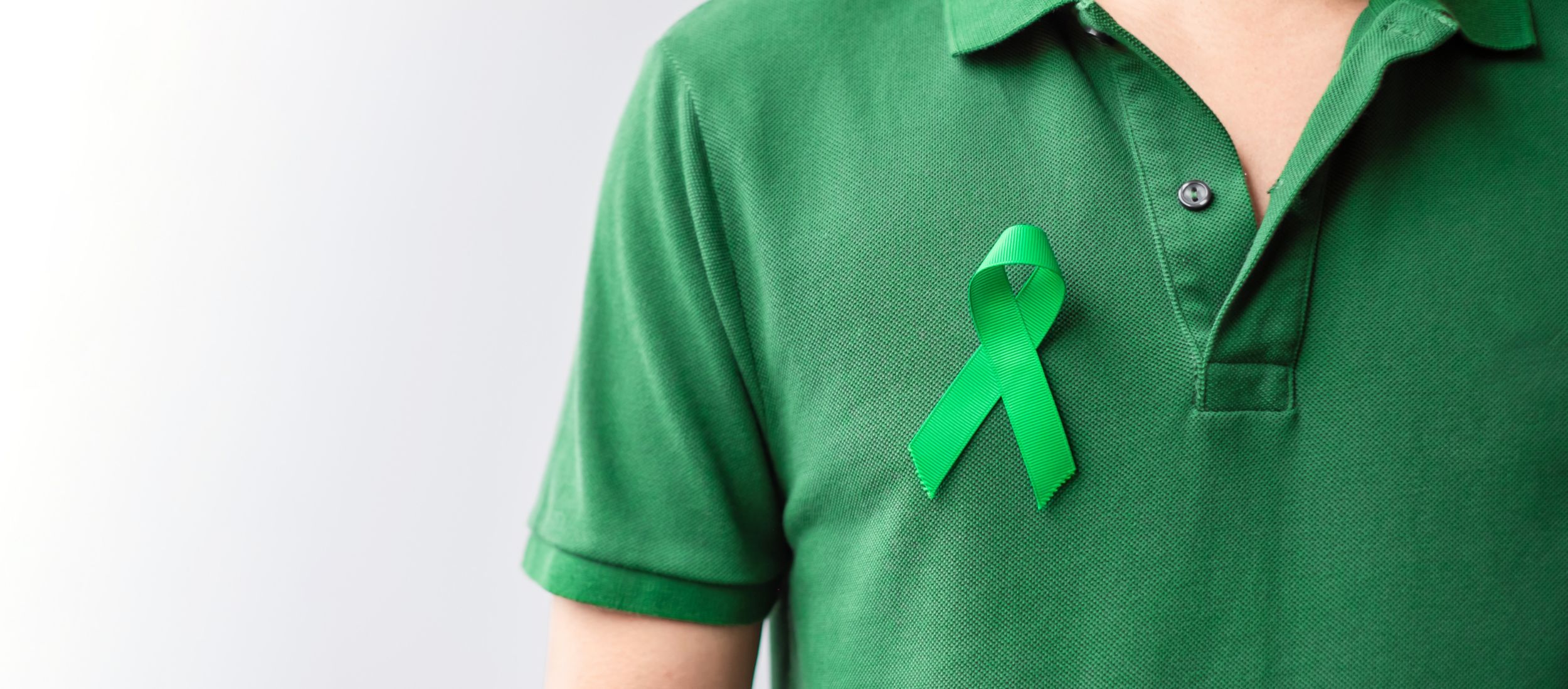 A closeup of a person wearing a green polo shirt with a bright green ribbon to represent mental health awareness