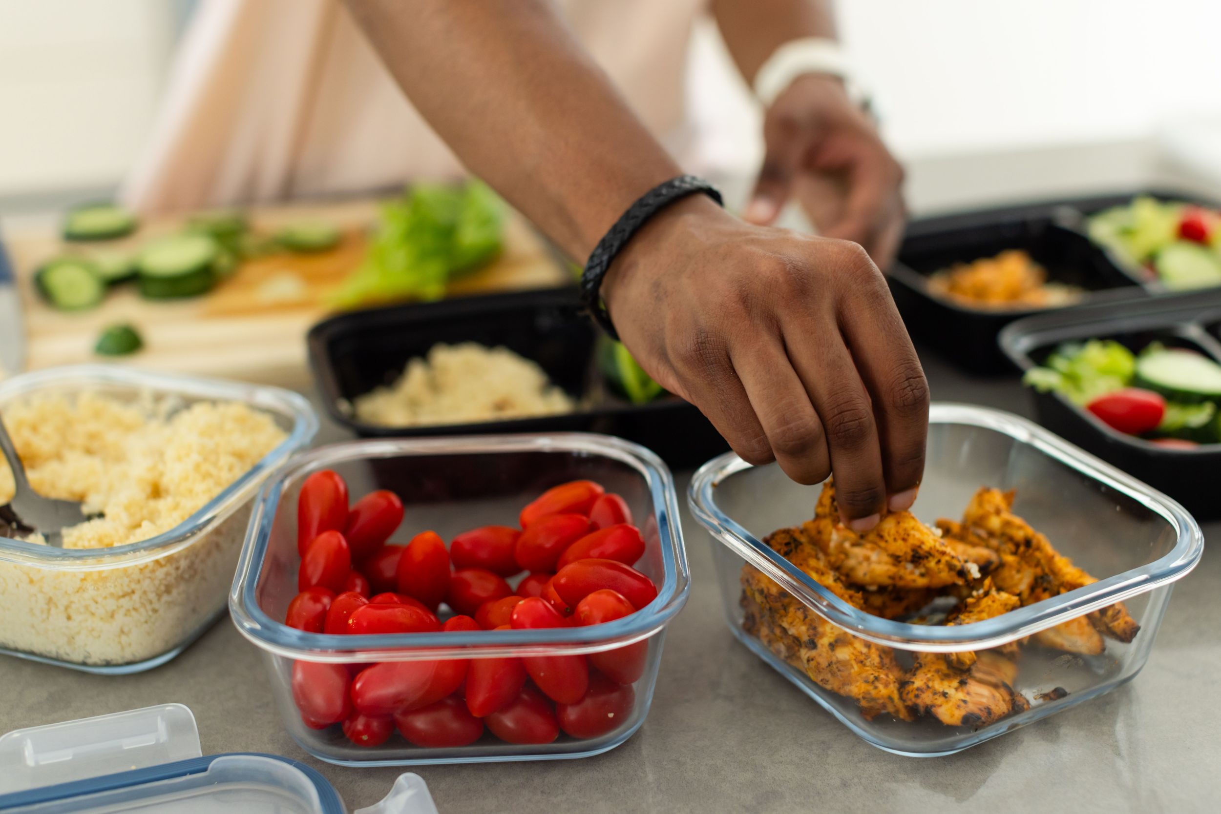 Hands preparing a healhy meal of seasoned chicked, tomatoes, whole grains, and cucumbers