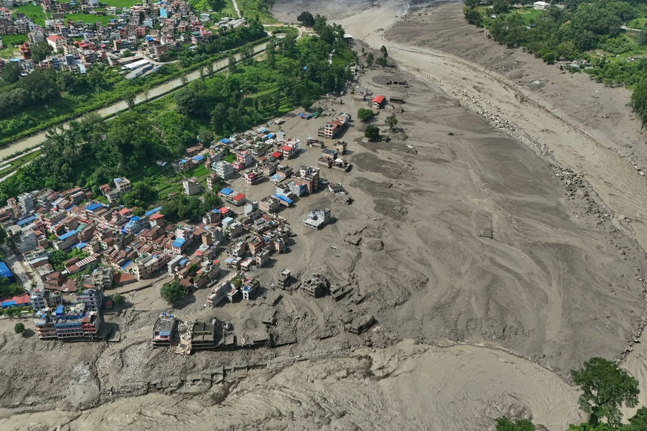 Damaged houses stand precariously near the swollen, debris-choked banks of the Trishuli River after flash floods in Nepal’s Nuwakot district on Wednesday, Aug. 26, 2026.