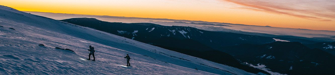 Two people hike up a snowy mountainside. 