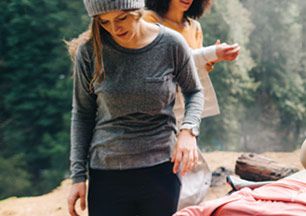 A woman wearing a lightweight base layer stands near a campsite. 
