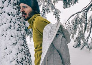A man wearing a mid-layer in the snowy woods. 
