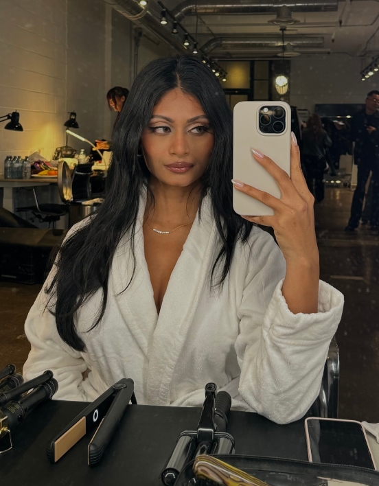 Krishna taking a selfie while wearing a white robe with makeup in front of her.