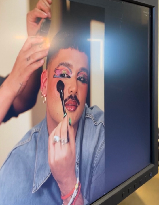A close-up of a monitor on set showing Michael applying makeup with a brush on camera.