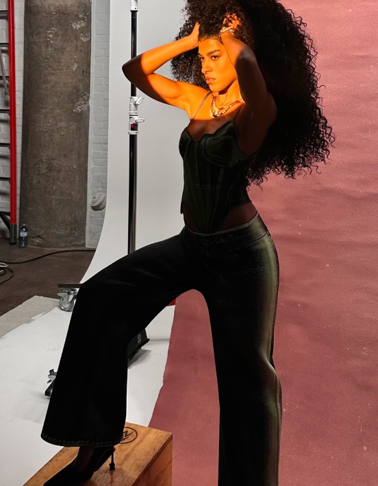 Samantha striking a pose on set, showing off her look of a green tank top and flared denim.